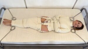 Cindy is chained to the bed in a straitjacket and straitjackets