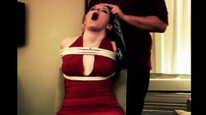 Caroline comes to, tied to a chair and roped around her torso